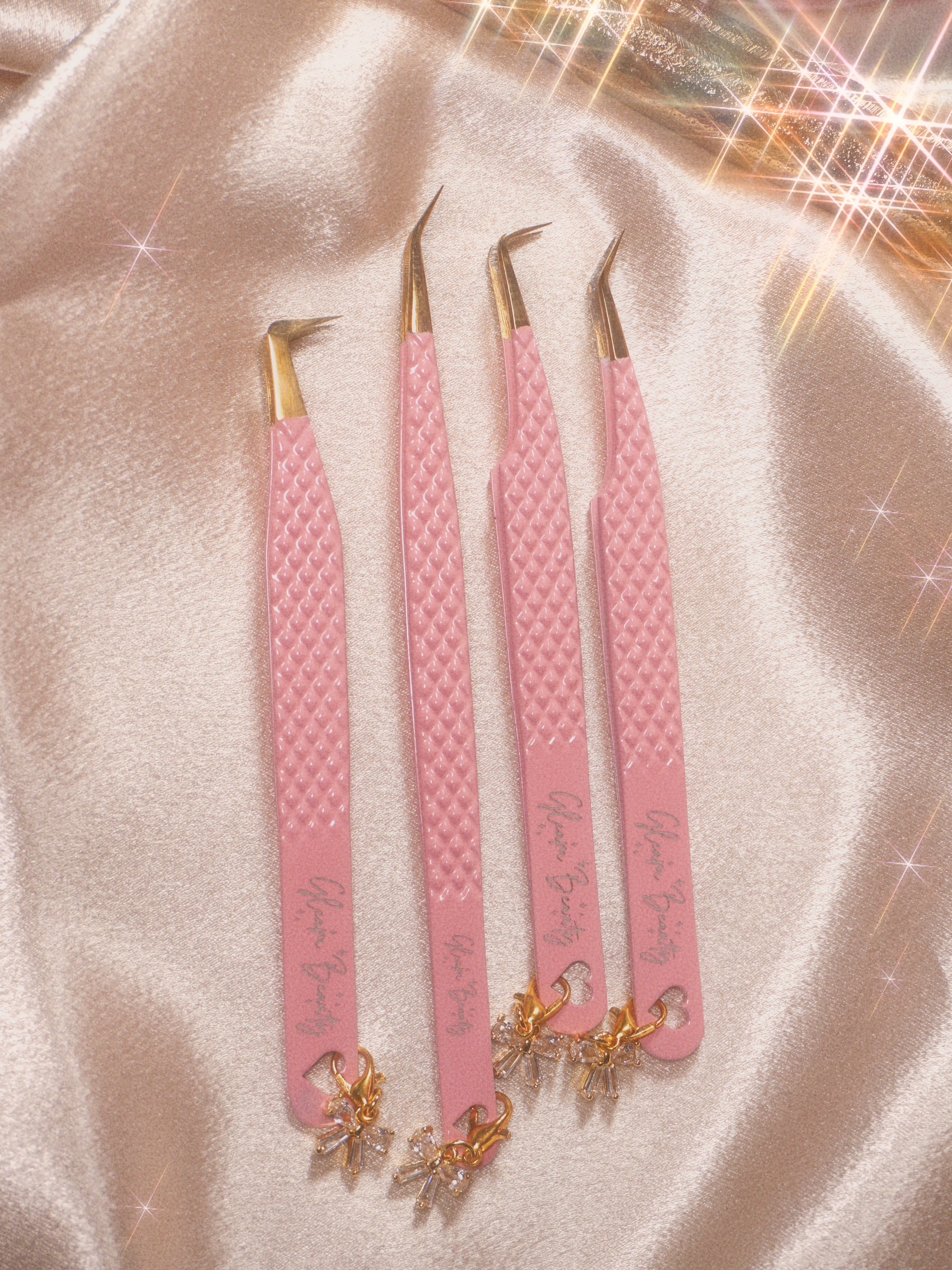 Set of pink tweezers with gold accents on a soft pink background